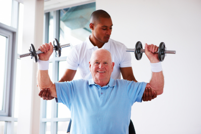 gym trainer guiding an elderly man as he performs presses with dumbbells
